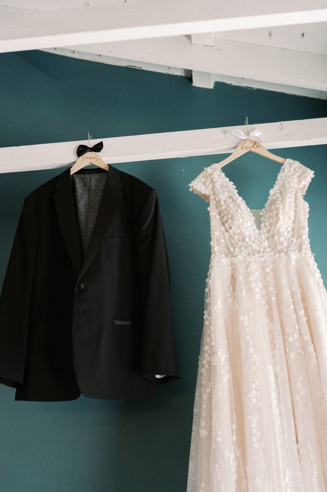 A wedding dress and a tuxedo hanging side by side on a teal wall
